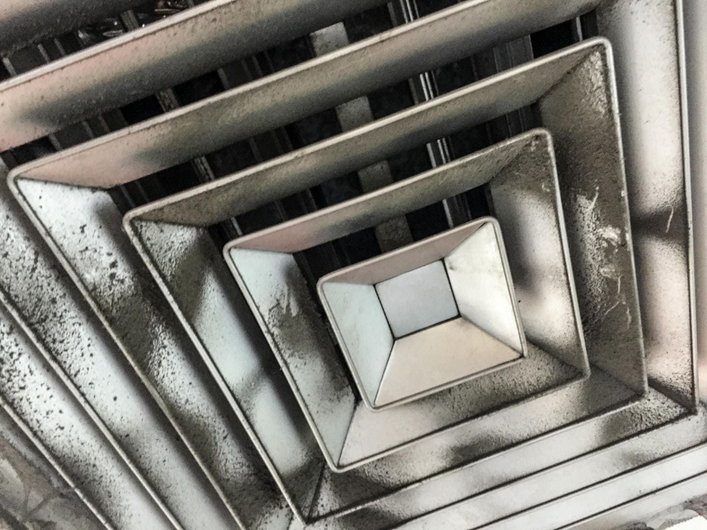 A close up of a dirty air vent on a ceiling.